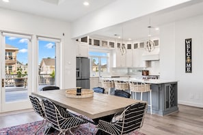 A modern kitchen with white cabinets, a stainless steel refrigerator, and a dining area with a wooden table and chairs.