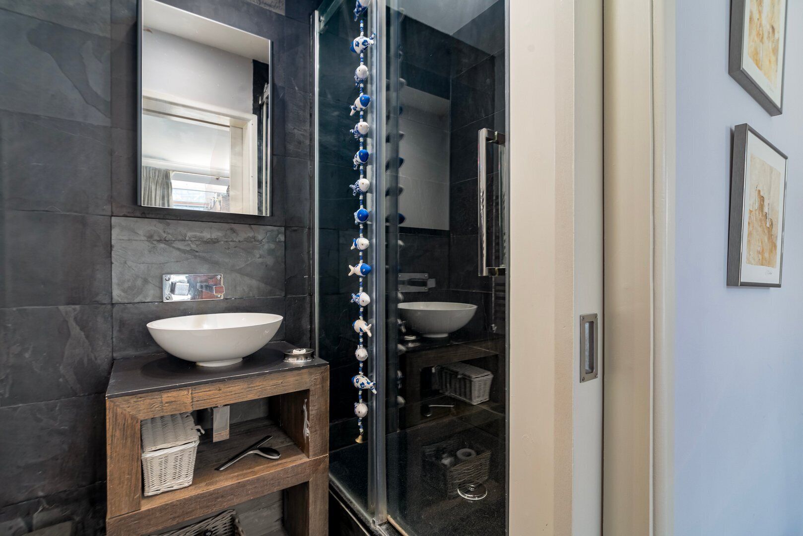 A modern bathroom with a large white sink, dark marble walls, and a wooden vanity.