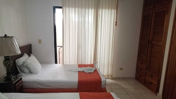 Ein Hotelzimmer mit zwei Betten, einem Nachttisch mit Lampe, einem Fenster mit Vorhängen und einem Holzschrank.