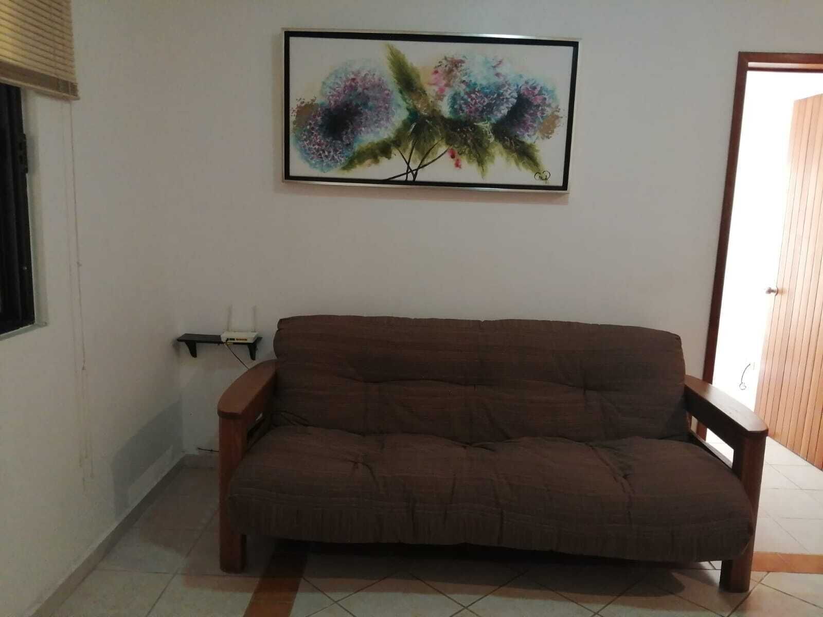 A living room with a brown sofa, a framed abstract painting, and a window with blinds.