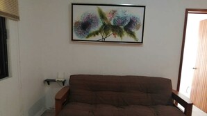 Ein Wohnzimmer mit einem braunen Sofa, einem gerahmten abstrakten Gemälde und einem Fenster mit Jalousien.