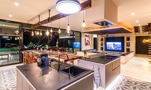 Uma cozinha moderna com ilha central, eletrodomésticos embutidos e iluminação pendente.