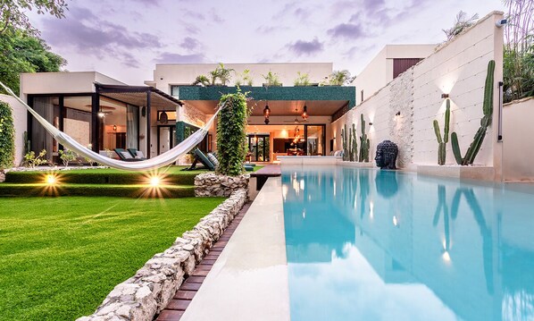 Uma casa moderna com piscina, rede e cactos.