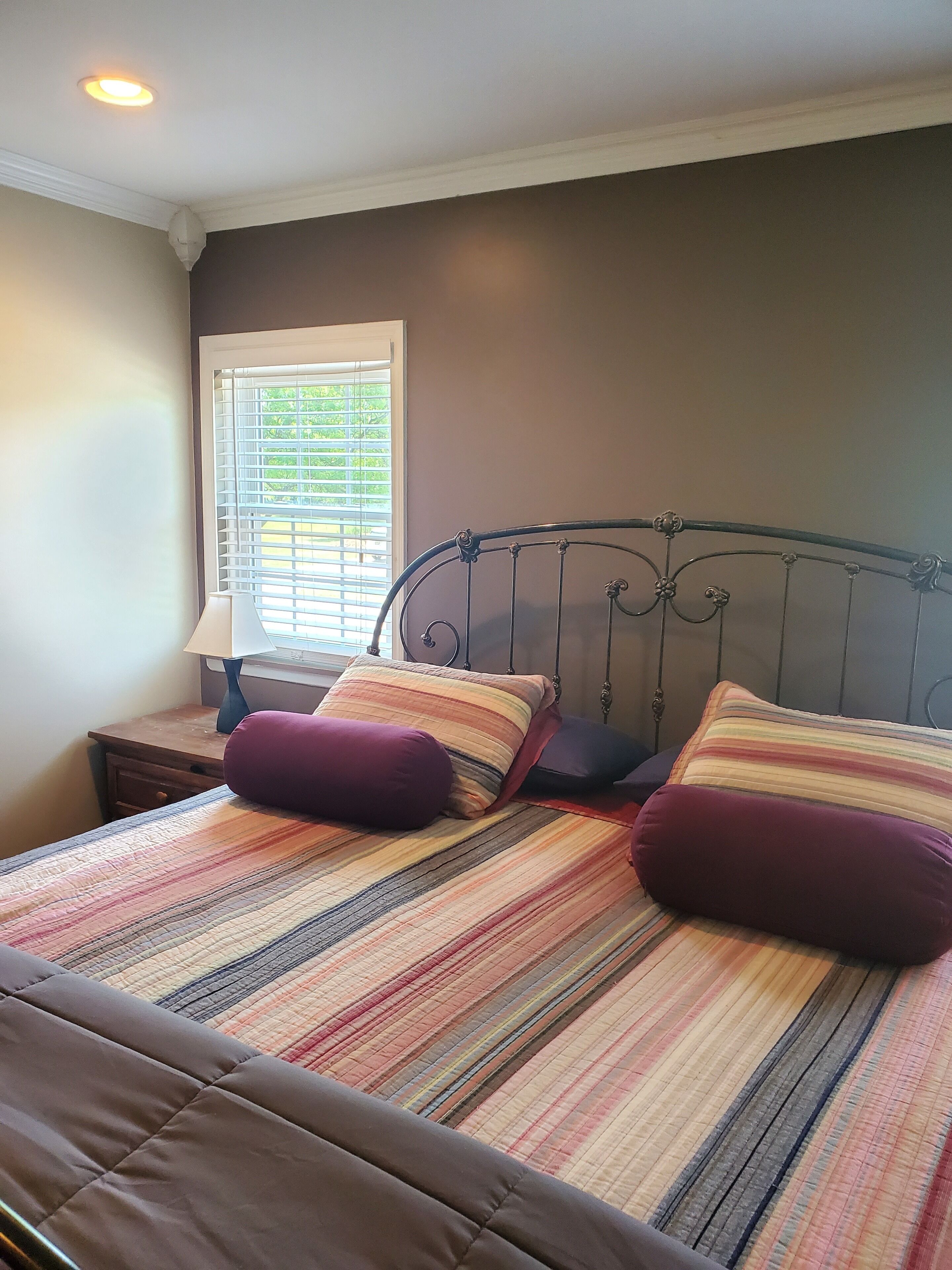 Un dormitorio con cama, mesita de noche, lámpara y ventana con persianas.