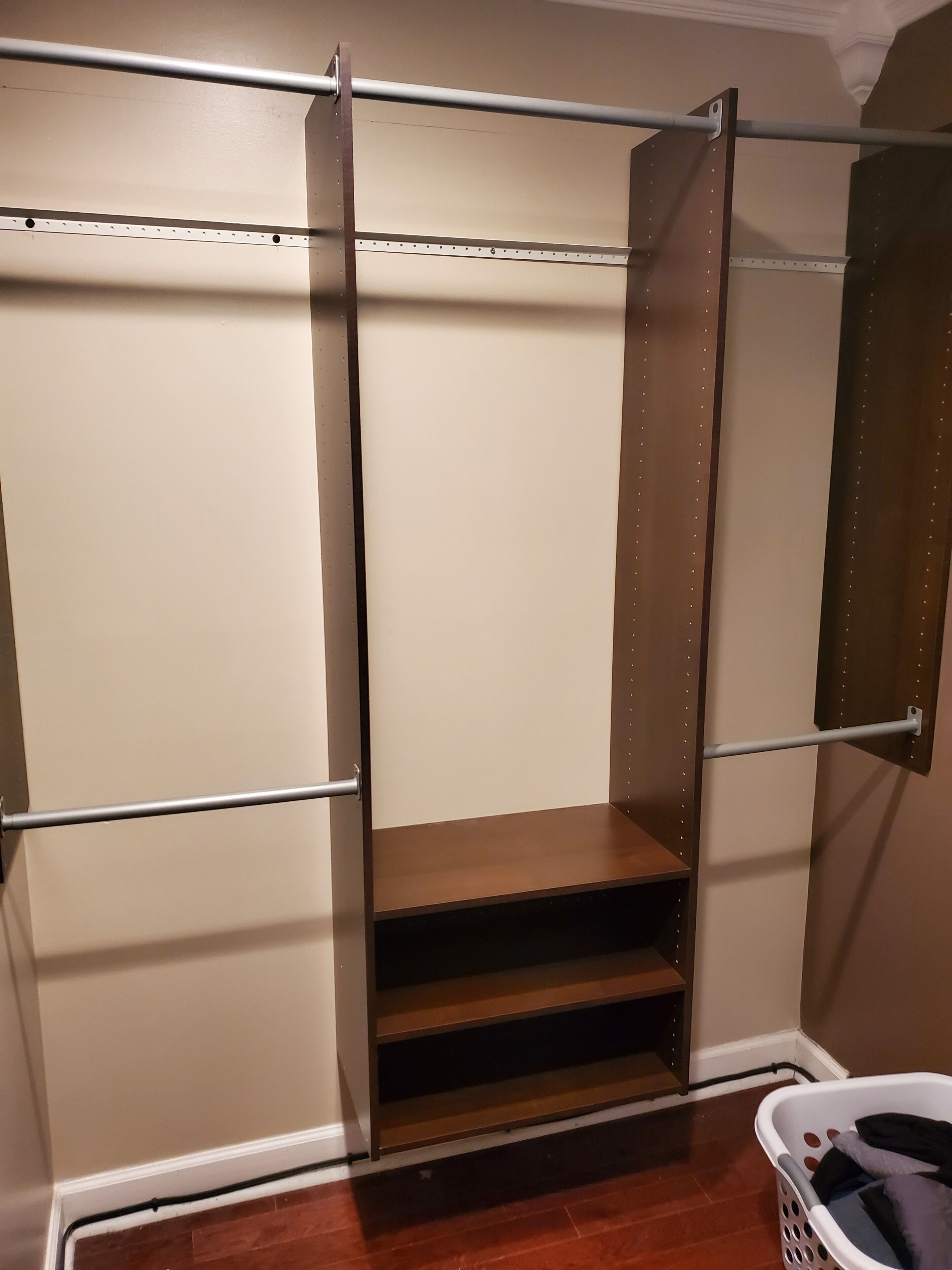 Ein begehbarer Kleiderschrank mit Metallstange, einem Holzpodest und einem Wäschekorb.
