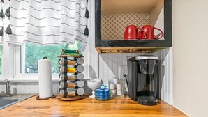 Una cocina con encimera de madera, cafetera, dispensador de toallas de papel y estante con tazas rojas.
