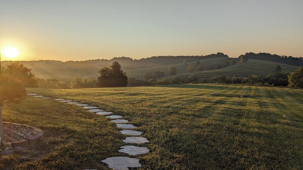 Un sendero que atraviesa un campo cubierto de hierba con un atardecer al fondo.