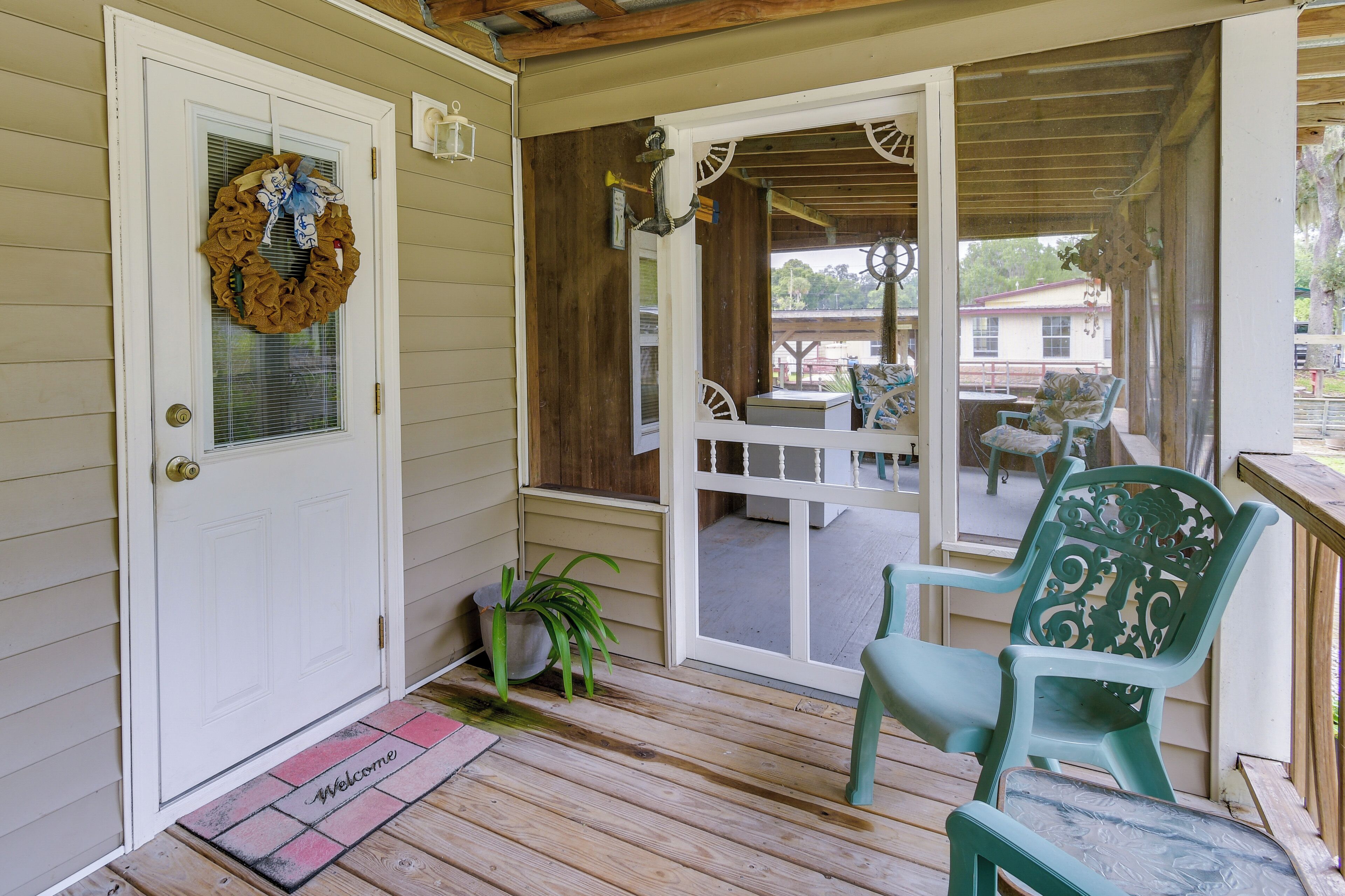 A wooden porch with a welcome mat, a green chair, and a door with a wreath.