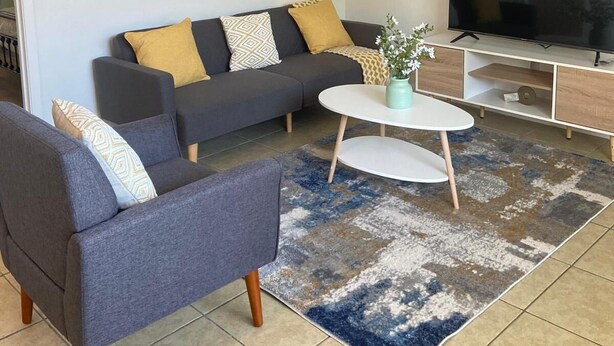 Ein modernes Wohnzimmer mit Sofa, Sessel, Couchtisch, TV-Möbel und Kunstwerk an der Wand.