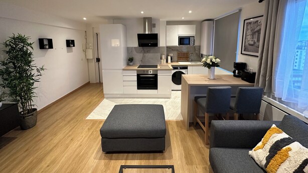 A modern apartment with a kitchen, dining area, and living room. It includes a sofa, a coffee table, and a dining table with chairs. - Charmant Appart Neuf Métro Proche Confort (Bagnolet)