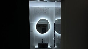 A modern bathroom with a round mirror, a sink, and a toilet. - Charmant Appart Neuf Métro Proche Confort (Bagnolet)