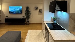 A modern kitchen with a built-in stove, a flat-screen TV, and a dining area with a bench. - Charmant Appart Neuf Métro Proche Confort (Bagnolet)