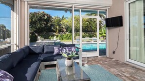 Ein sonnendurchflutetes Wohnzimmer mit großem Fenster, Pool und Wandfernseher.