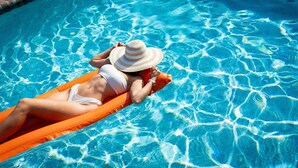 Eine Person liegt auf einem orangefarbenen Schwimmpfiff in einem klaren, blauen Pool.