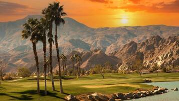 A golf course with palm trees, a lake, and mountains in the background.