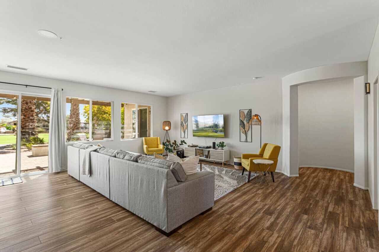 A modern living room with a sectional sofa, yellow chairs, a dining area, and large windows.