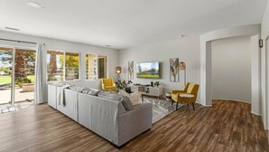Ein modernes Wohnzimmer mit einer Eckcouch, gelben Sesseln, einem Essbereich und großen Fenstern.