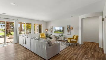 A modern living room with a sectional sofa, yellow chairs, a dining area, and large windows.