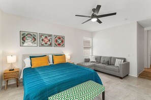 A bedroom with a bed, a gray sofa, a ceiling fan, and wall art. - Coachella Music Festival 10min walk to grounds (Indio)