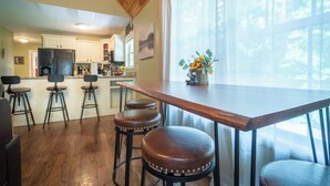 Una cocina con taburetes de madera, una mesa de madera y una ventana con vistas a árboles.