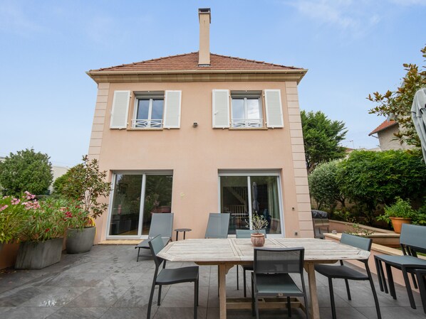 A two-story house with a tiled roof, a balcony, and a patio with a table and chairs.