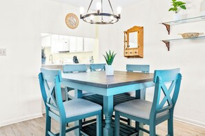 Un coin repas avec une table ronde, des chaises bleues, un lustre, un buffet en bois et une plante en pot.