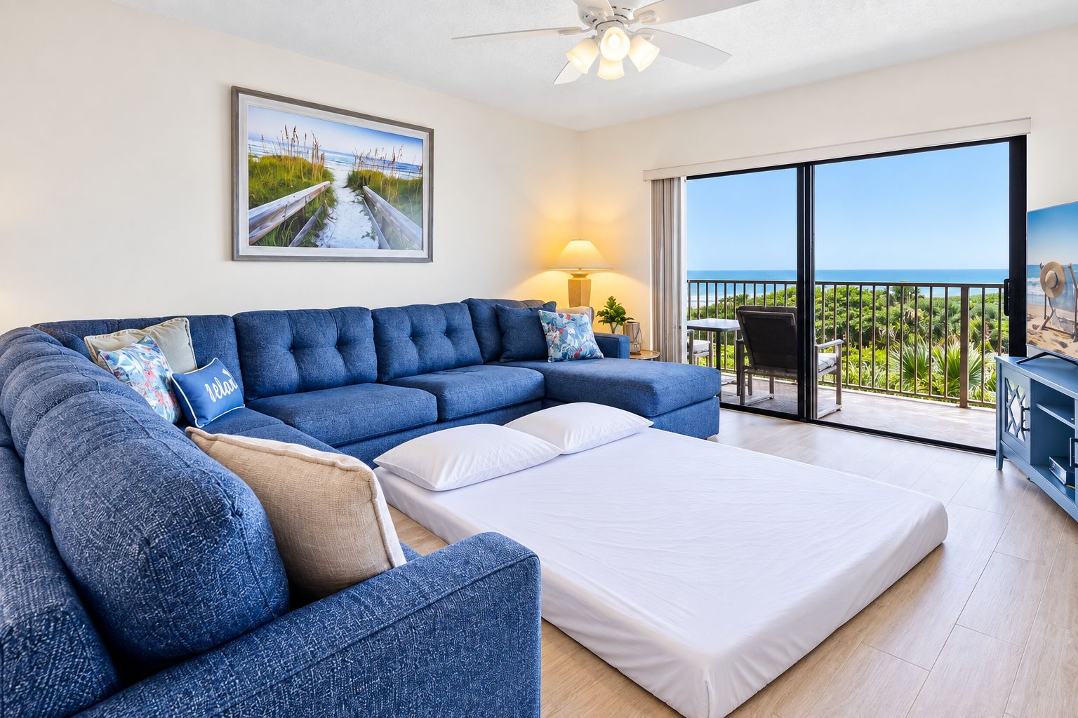 A modern living room with a sectional sofa, a flat-screen TV, and a balcony with a view of the ocean.