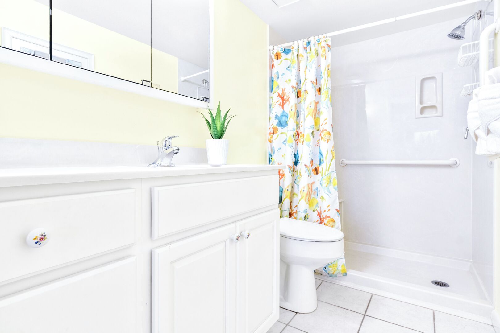 Un baño moderno con un tocador blanco, una ducha con cortina colorida y una planta en maceta.
