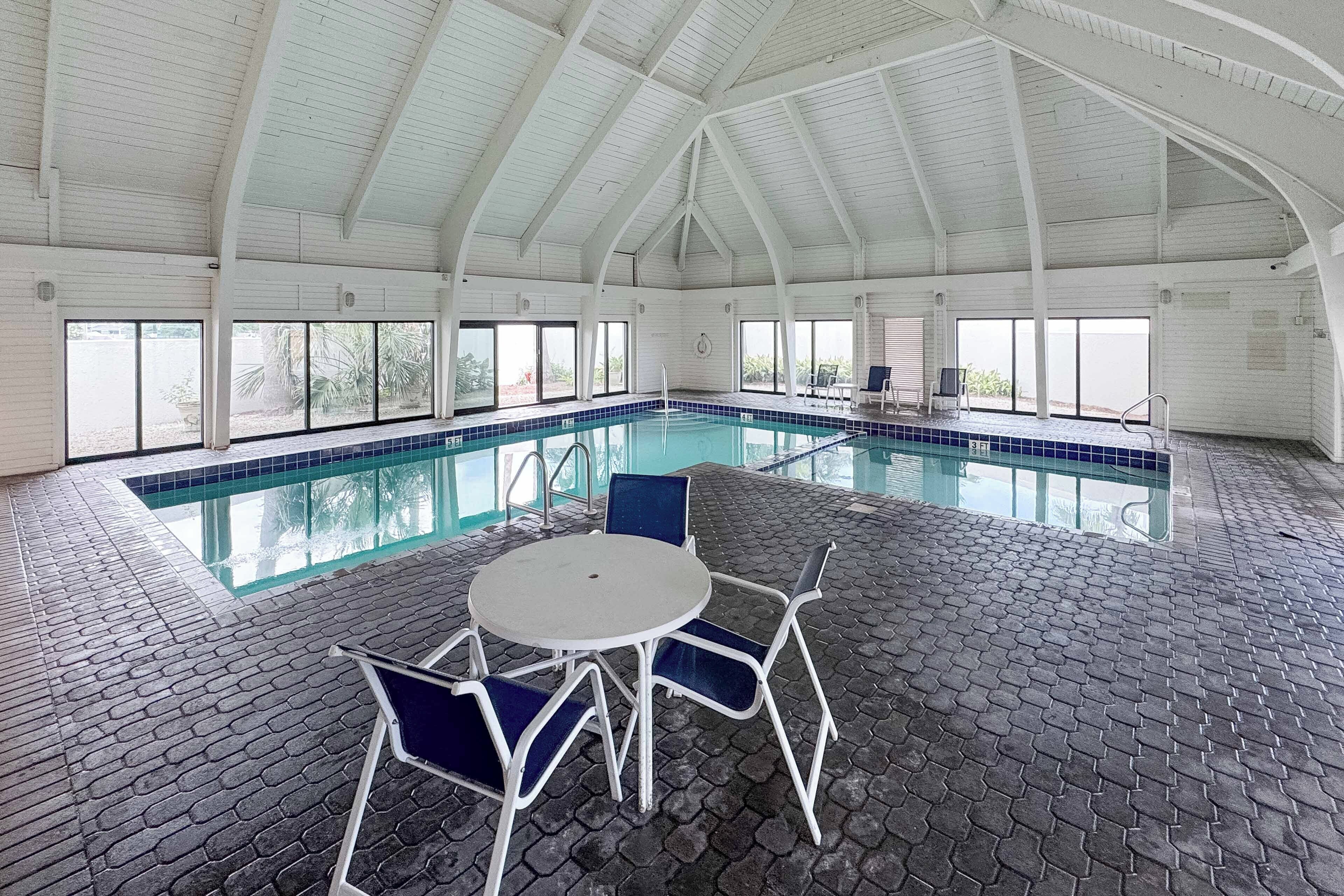 An indoor swimming pool with a tiled floor, a white ceiling, and large windows.