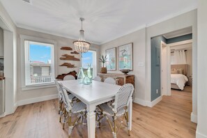Un coin repas avec une table blanche, des chaises en osier et un lustre.