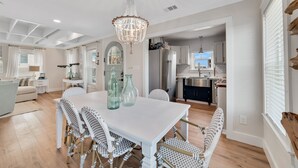 Uma sala de estar ampla com uma mesa de jantar branca, cadeiras estampadas e um candelabro.
