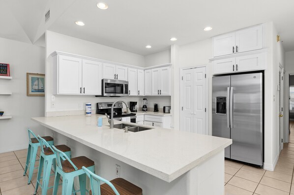 A modern kitchen with white cabinets, stainless steel appliances, and a central island with bar stools.