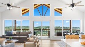 Ein geräumiger Wohnbereich mit großem Fenster und Blick auf eine reizvolle Landschaft, einem Deckenventilator und einem Essbereich mit Sitzgelegenheiten im Freien.