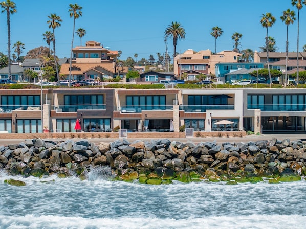 A coastal hotel with modern architecture, featuring multiple stories, large windows, and a view of the ocean.