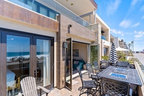 A modern hotel with a glass balcony overlooking the ocean, furnished with outdoor seating and a table.