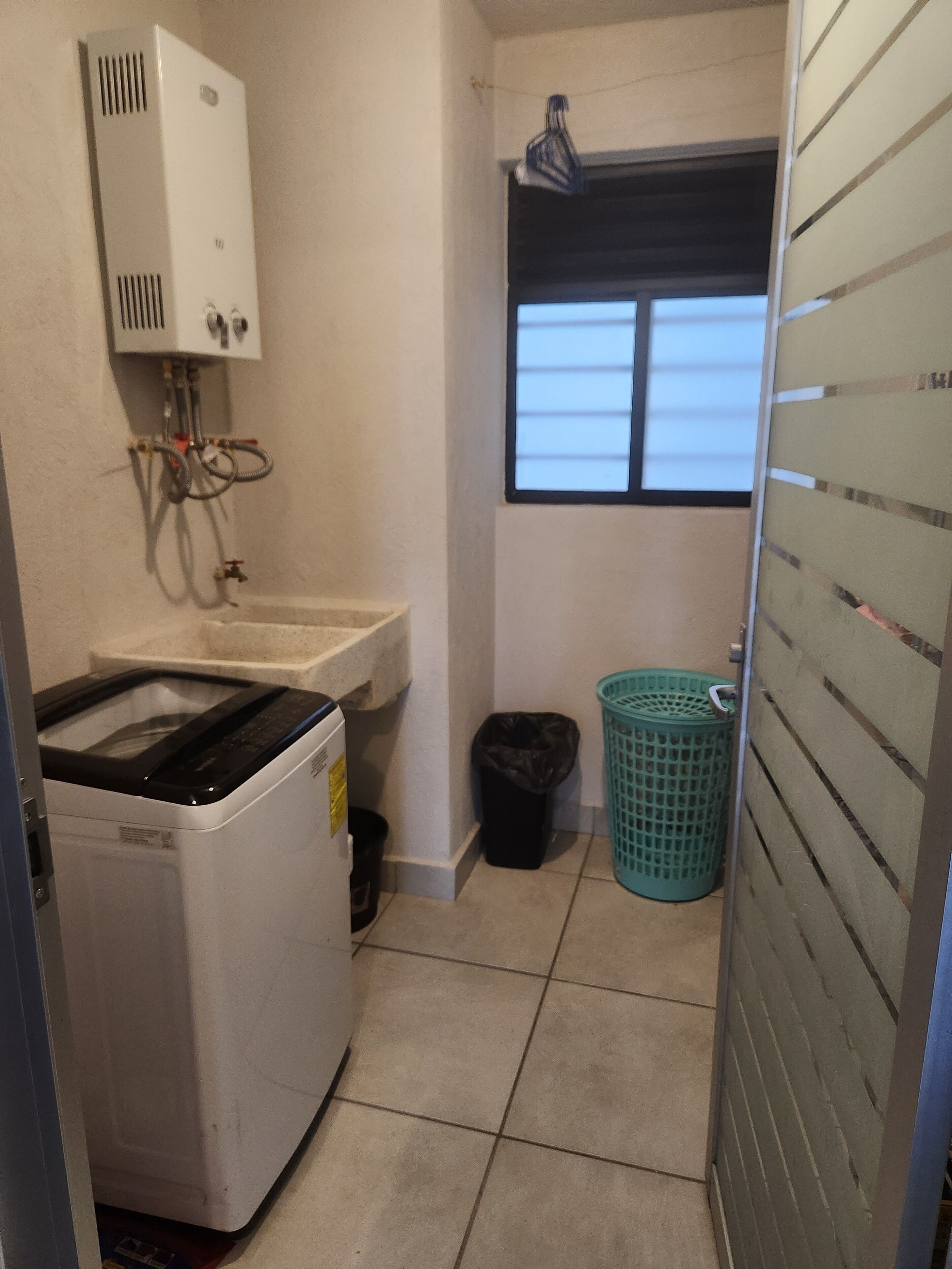 Una sala de lavandería con lavadora, lavabo, ventana y cubo de basura.