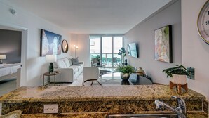 A modern kitchen with granite countertops, a sink, and a dining area with a table and chairs. There is a large window providing natural light and a view of the outdoors. - Direct Bayview One Bedroom Condo in Coconut Grove-includes parking (Coconut Grove)