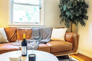 A living room with a brown leather sofa, a round coffee table, a bottle of wine, and two wine glasses. - Cozy- Stylish 2 bd with fenced in back yard w/ Firepit (Ferndale)