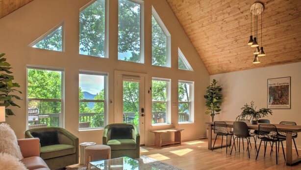 Amplia sala de estar con ventanas grandes, techo de madera y un comedor con sillas y una mesa.