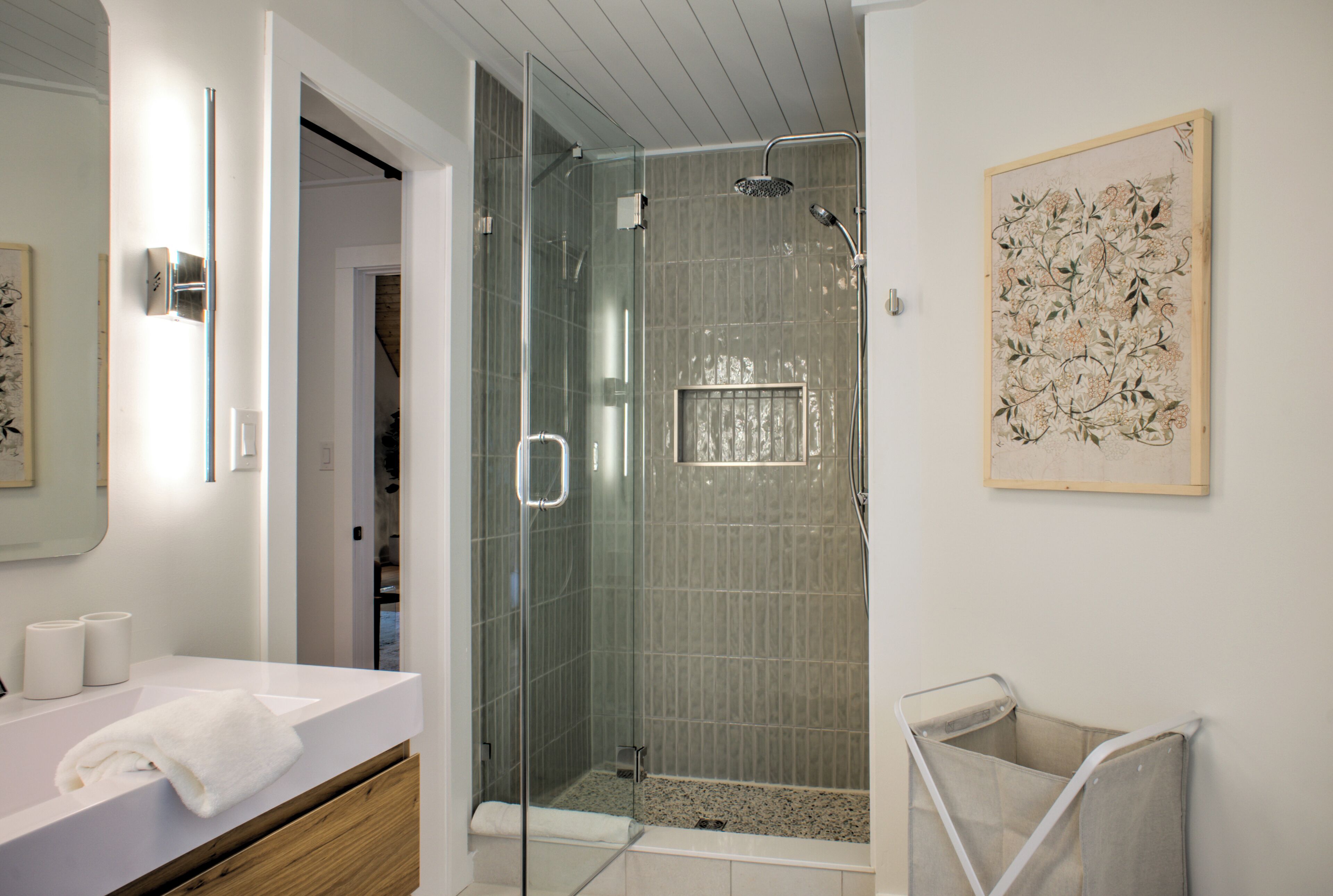 Een moderne badkamer met een douchecabine van glas, een witte wastafel en een bloemrijk kunstwerk in een lijst aan de muur.