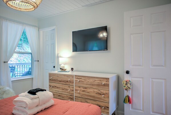 A bedroom with a bed, a dresser, a TV mounted on the wall, and a window with curtains. - The Honeybee Hideaway | A Peaceful Sanctuary | Hot Tub, Fire Pit and Pet-Friendly (Weaverville)