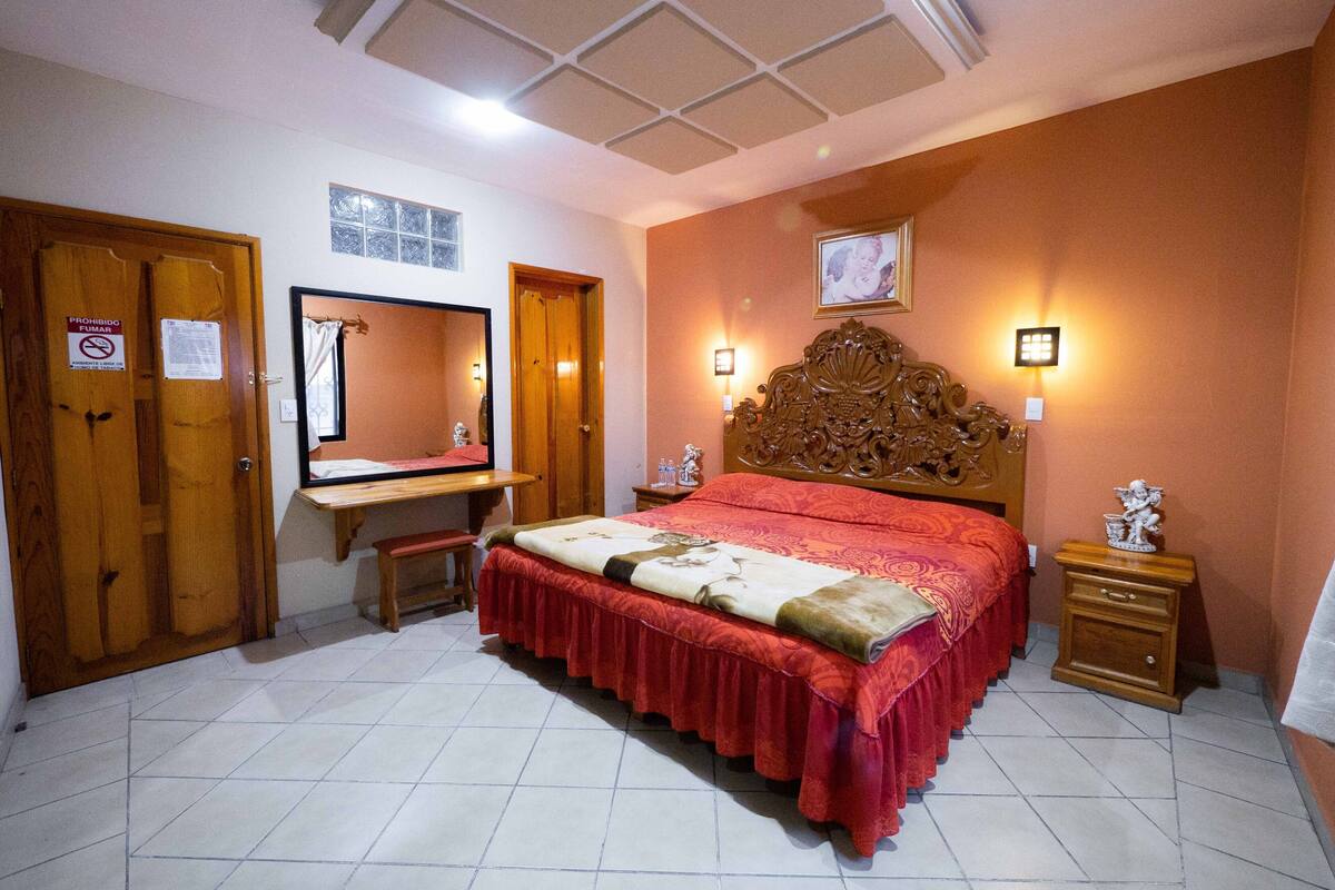 A bedroom with a bed, a desk, a chair, a mirror, and a nightstand.