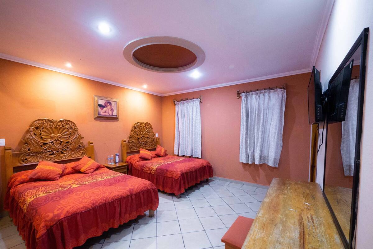 A hotel room with two beds, a wooden headboard, a small table, a mirror, and a television.