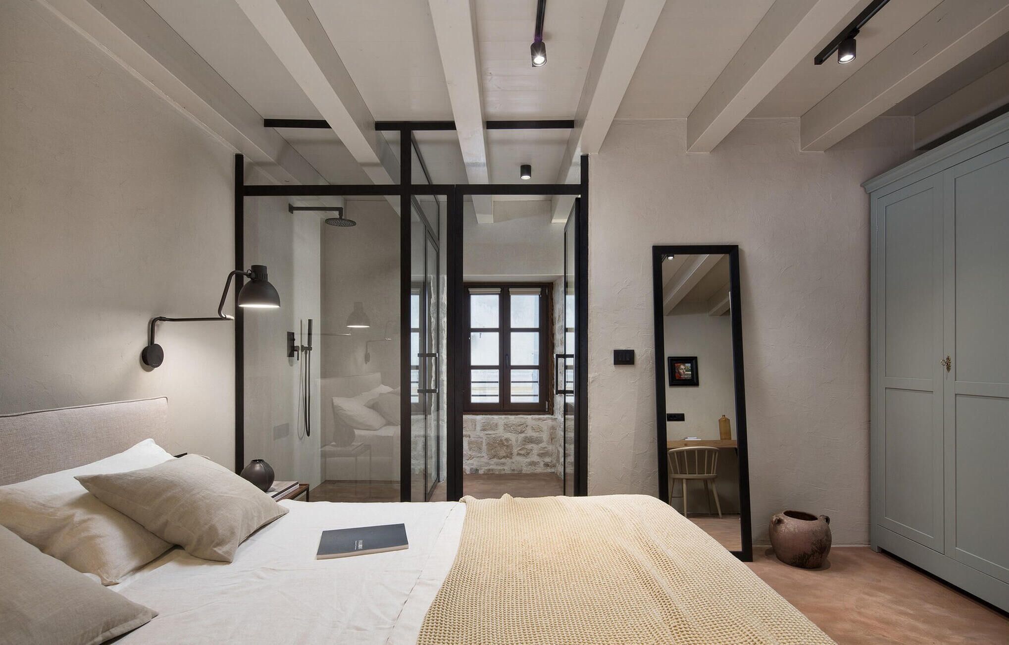 A bedroom with a bed, a bedside lamp, a mirror, and a wardrobe.