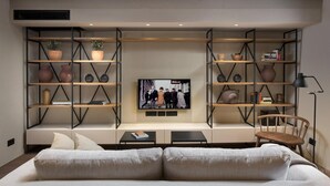 Una sala de estar moderna con un sofá, un televisor montado en la pared y estanterías empotradas con objetos decorativos.