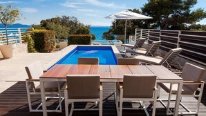 A poolside area with a wooden deck, lounge chairs, and a table. - Beach front home in Petrcane (Petrcane)