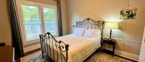 A bedroom with a bed, a nightstand, a lamp, a window with curtains, and a ceiling fan.