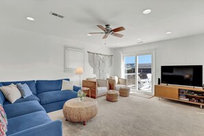 A living room with a blue sofa, a wooden coffee table, a television, and a ceiling fan. - Steps to the beach. Canal front with new dock. Clean, Cozy Getaway.   (Surf City)