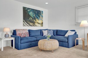 A blue sofa, a woven ottoman, a lamp, and a painting on the wall. - Steps to the beach. Canal front with new dock. Clean, Cozy Getaway.   (Surf City)