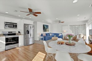 A modern kitchen with built-in appliances, a dining area with a marble table, and a living space with a blue sofa. - Steps to the beach. Canal front with new dock. Clean, Cozy Getaway.   (Surf City)